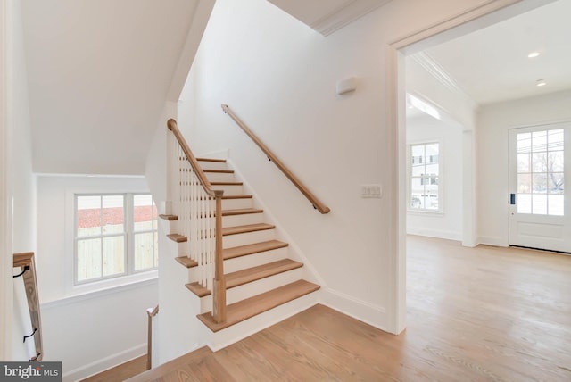 stairway featuring a wealth of natural light, wood-type flooring, and ornamental molding