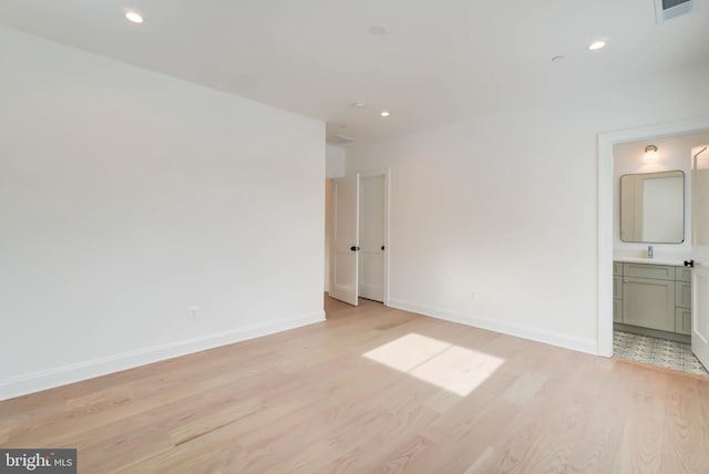 unfurnished bedroom featuring ensuite bath, sink, and light wood-type flooring