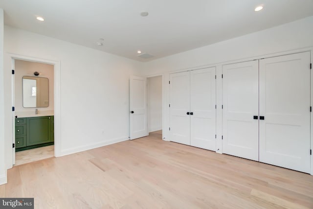 unfurnished bedroom featuring connected bathroom, light hardwood / wood-style floors, multiple closets, and sink