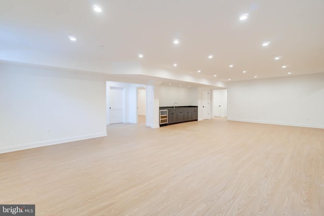 unfurnished living room with sink, beverage cooler, and light hardwood / wood-style flooring