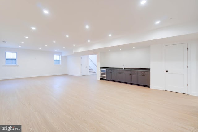 basement with light wood-type flooring, beverage cooler, and sink