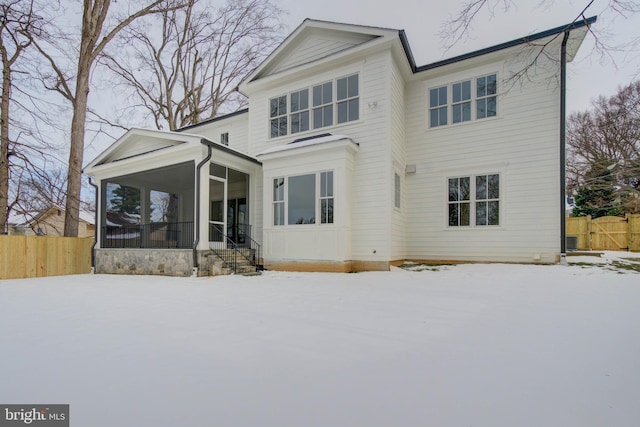 snow covered back of property with a sunroom