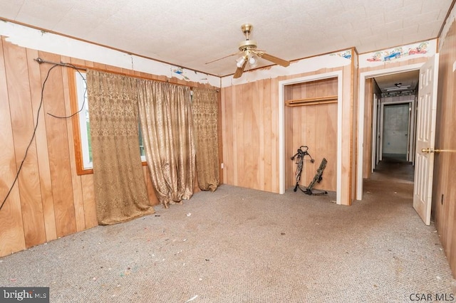 unfurnished bedroom with carpet, ceiling fan, wood walls, and a closet