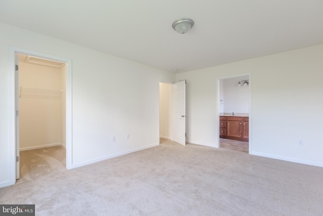 unfurnished bedroom with light colored carpet, a spacious closet, ensuite bathroom, and a closet