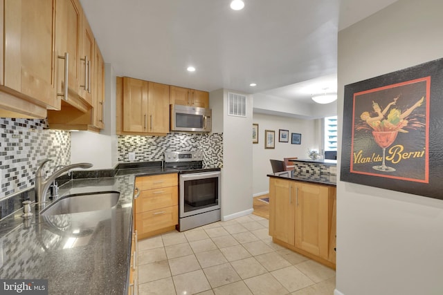 kitchen with sink, stainless steel appliances, light tile patterned flooring, dark stone countertops, and light brown cabinets