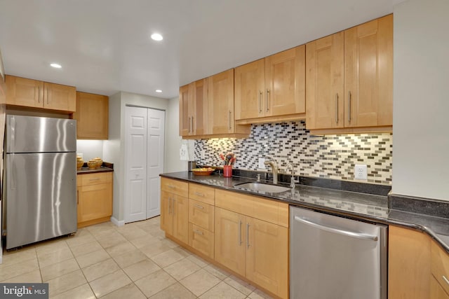 kitchen with dark stone countertops, stainless steel appliances, light brown cabinets, sink, and backsplash