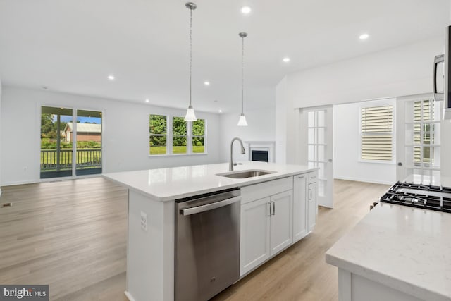 kitchen with stainless steel dishwasher, sink, white cabinetry, hanging light fixtures, and an island with sink