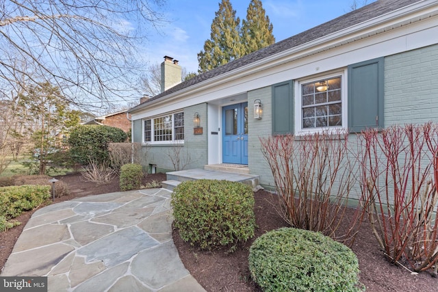 doorway to property featuring brick siding and a chimney