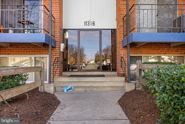 view of exterior entry featuring brick siding and a balcony