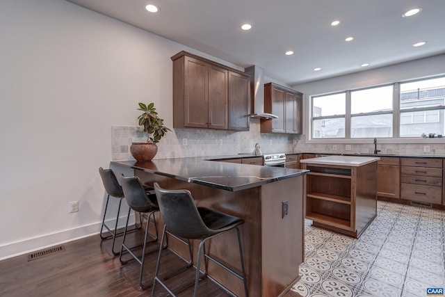 kitchen with a breakfast bar area, stainless steel electric range, kitchen peninsula, wall chimney exhaust hood, and sink