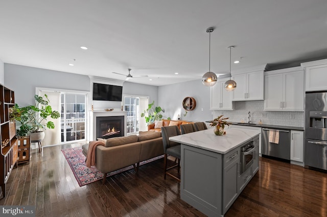 kitchen featuring decorative light fixtures, tasteful backsplash, a center island, white cabinetry, and appliances with stainless steel finishes