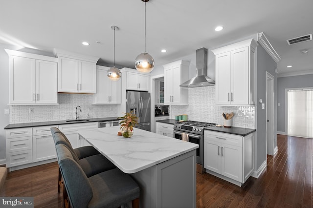 kitchen featuring pendant lighting, sink, white cabinetry, appliances with stainless steel finishes, and wall chimney exhaust hood