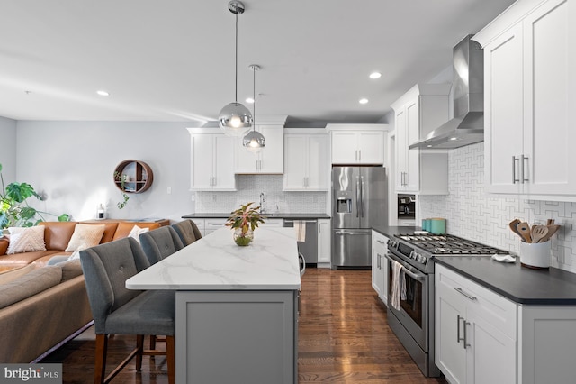 kitchen featuring white cabinetry, appliances with stainless steel finishes, dark stone countertops, wall chimney range hood, and pendant lighting