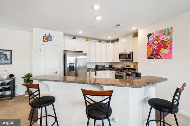 kitchen featuring light carpet, a kitchen breakfast bar, white cabinets, dark stone countertops, and stainless steel appliances