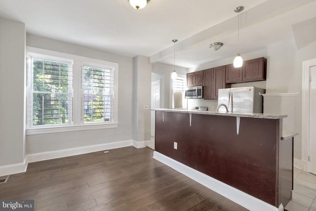 kitchen featuring a kitchen breakfast bar, light stone counters, decorative light fixtures, and appliances with stainless steel finishes