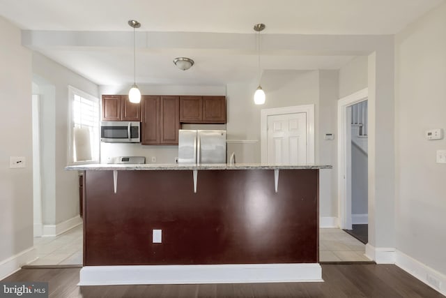 kitchen with a breakfast bar area, light hardwood / wood-style flooring, decorative light fixtures, and appliances with stainless steel finishes