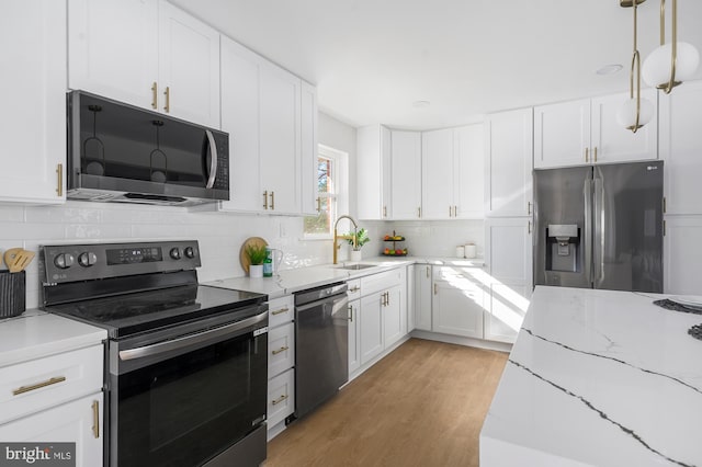 kitchen with light stone countertops, white cabinets, appliances with stainless steel finishes, decorative light fixtures, and sink