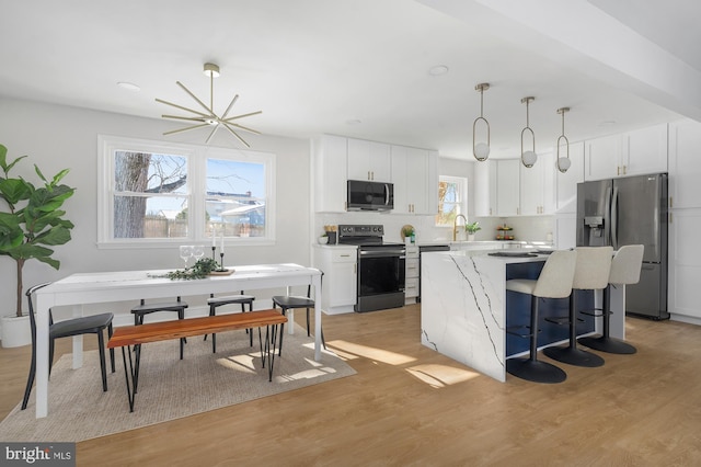 kitchen featuring white cabinetry, appliances with stainless steel finishes, light wood-type flooring, hanging light fixtures, and a kitchen island