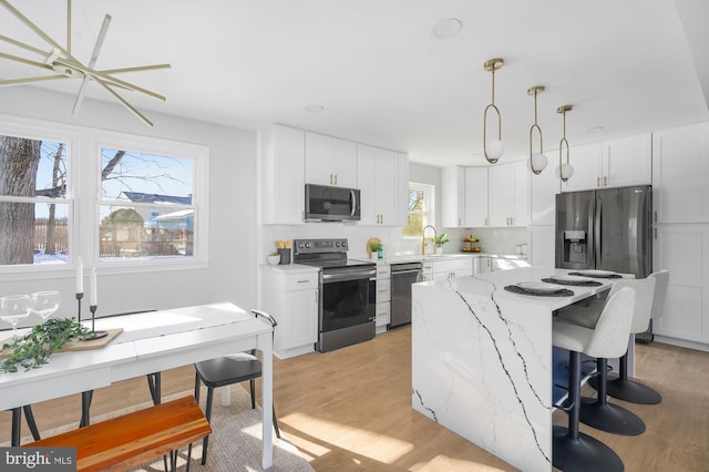 kitchen featuring white cabinetry, hanging light fixtures, light wood-type flooring, light stone countertops, and stainless steel appliances