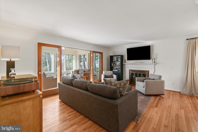 living area with crown molding, baseboards, a glass covered fireplace, and light wood-style floors