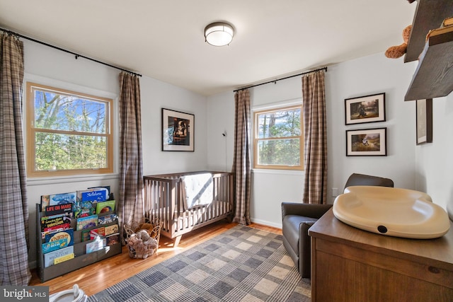 bedroom with a nursery area, baseboards, and wood finished floors