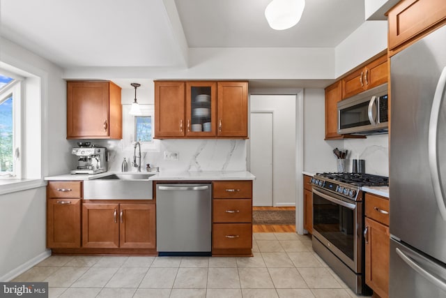 kitchen with stainless steel appliances, a sink, light countertops, brown cabinets, and tasteful backsplash