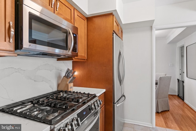 kitchen with light stone counters, brown cabinets, stainless steel appliances, backsplash, and baseboards