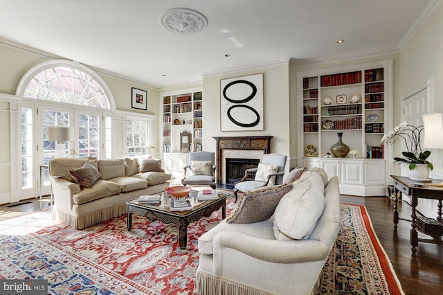 living room featuring dark wood-type flooring, built in shelves, crown molding, and a fireplace