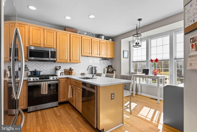 kitchen featuring sink, appliances with stainless steel finishes, decorative light fixtures, light hardwood / wood-style floors, and light stone counters