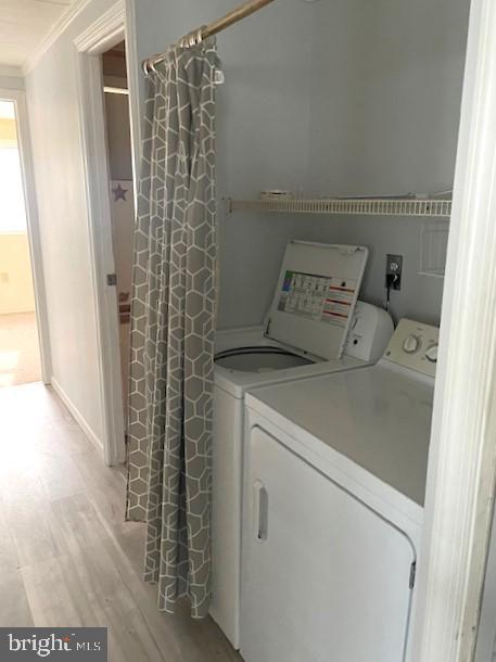 laundry room featuring crown molding, washer and clothes dryer, and light hardwood / wood-style floors