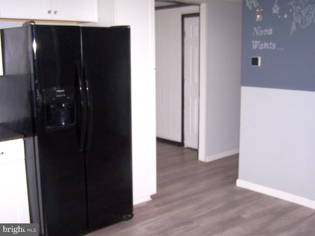 kitchen with black fridge, white cabinetry, and hardwood / wood-style flooring