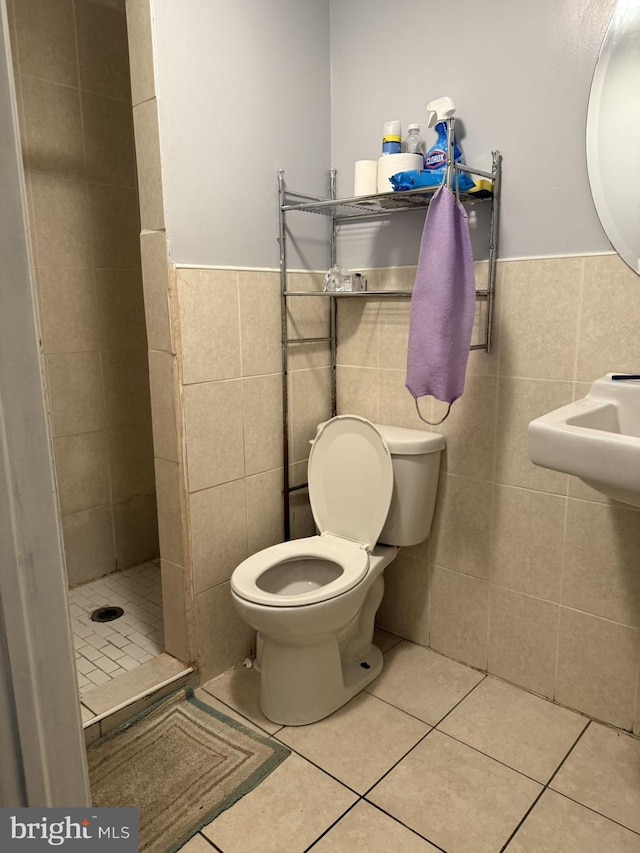 bathroom with tiled shower, tile patterned floors, toilet, and tile walls