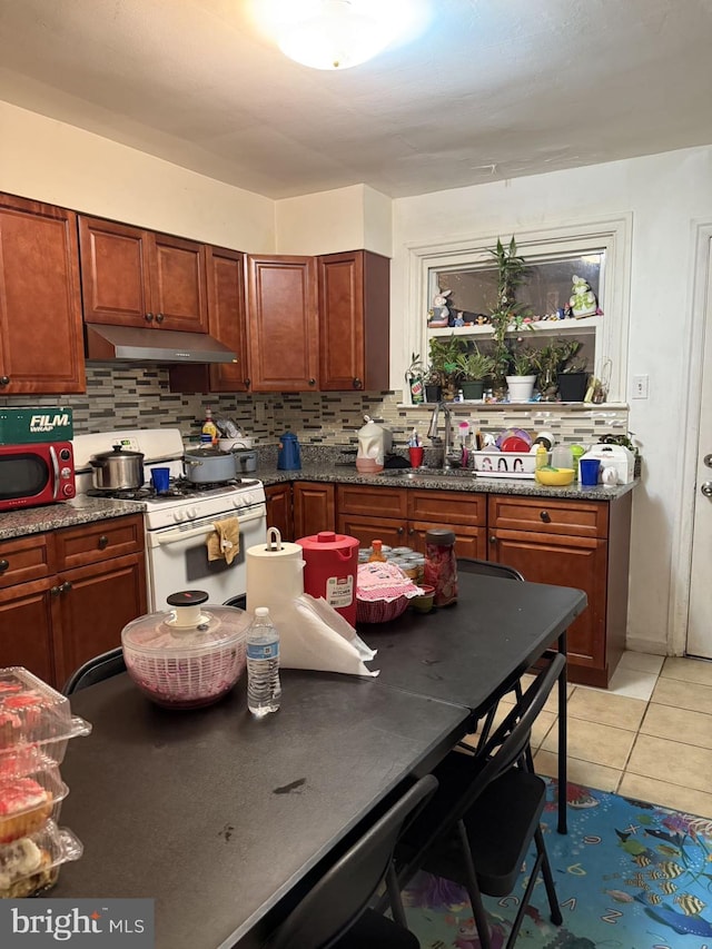 kitchen featuring white gas range, decorative backsplash, sink, and light tile patterned floors