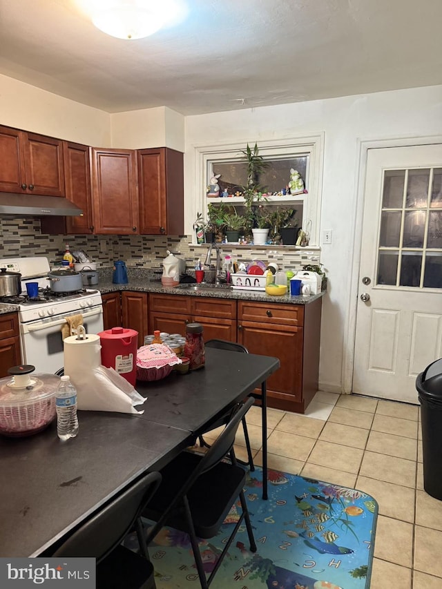 kitchen with backsplash, dark stone countertops, gas range gas stove, and light tile patterned flooring