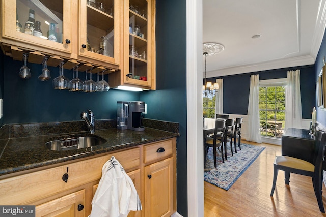 kitchen featuring sink, dark stone counters, hanging light fixtures, ornamental molding, and light hardwood / wood-style flooring