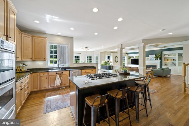 kitchen with ornate columns, a center island, light wood-type flooring, light brown cabinets, and stainless steel appliances