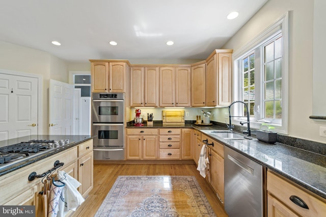 kitchen featuring stainless steel appliances, sink, dark stone counters, and light brown cabinets