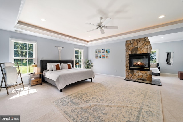 bedroom featuring a raised ceiling, a stone fireplace, light carpet, and ceiling fan