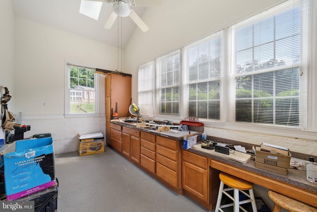 kitchen featuring ceiling fan, vaulted ceiling with skylight, and concrete flooring