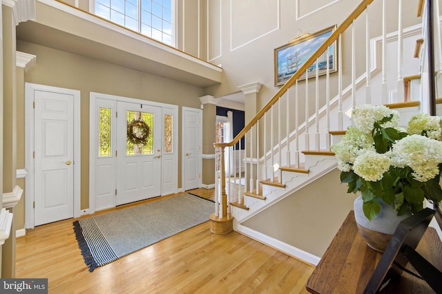 foyer entrance featuring a towering ceiling, decorative columns, and light hardwood / wood-style floors