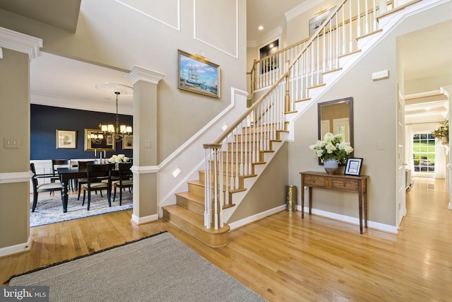 staircase featuring ornamental molding, a towering ceiling, hardwood / wood-style floors, and a chandelier