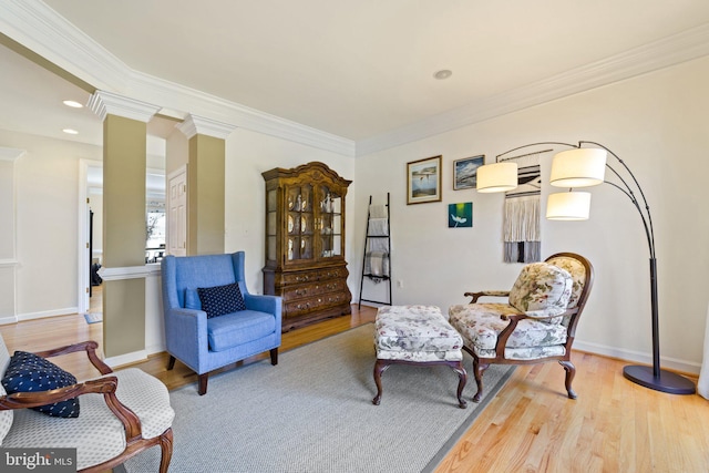 living area with crown molding, ornate columns, and light wood-type flooring