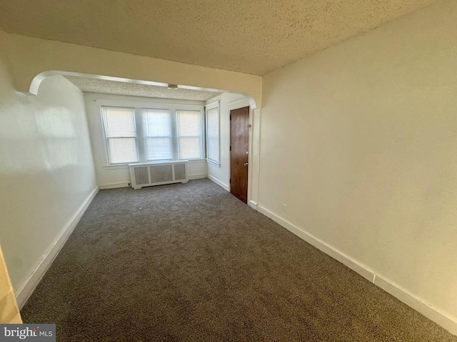 unfurnished room featuring a textured ceiling, dark carpet, and radiator