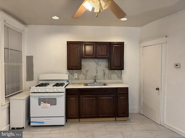 kitchen with backsplash, sink, ceiling fan, white gas range, and dark brown cabinets