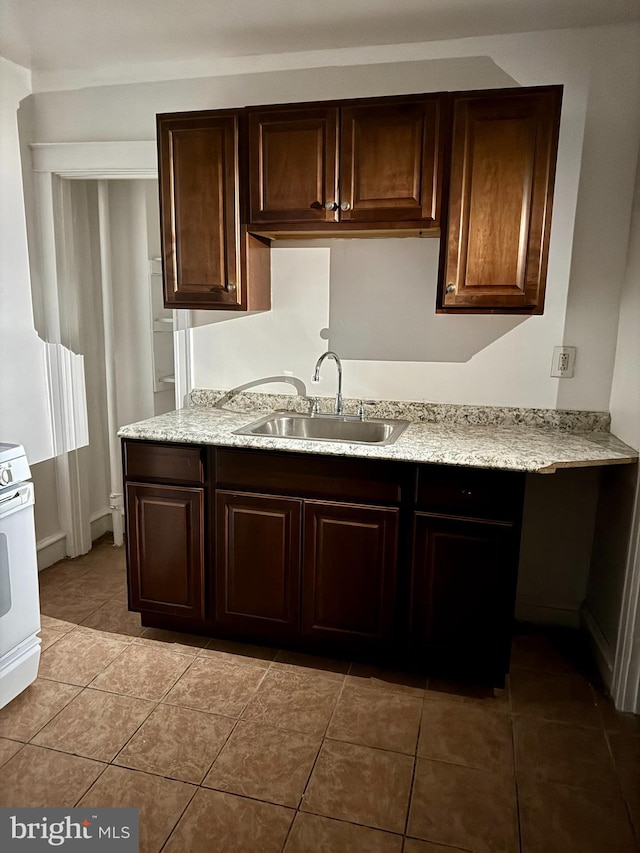 kitchen featuring white range oven, dark brown cabinetry, light tile patterned floors, and sink