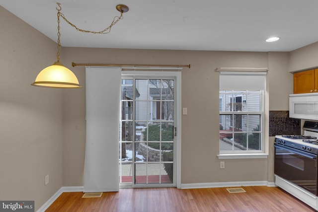 kitchen with white appliances, light hardwood / wood-style floors, and hanging light fixtures