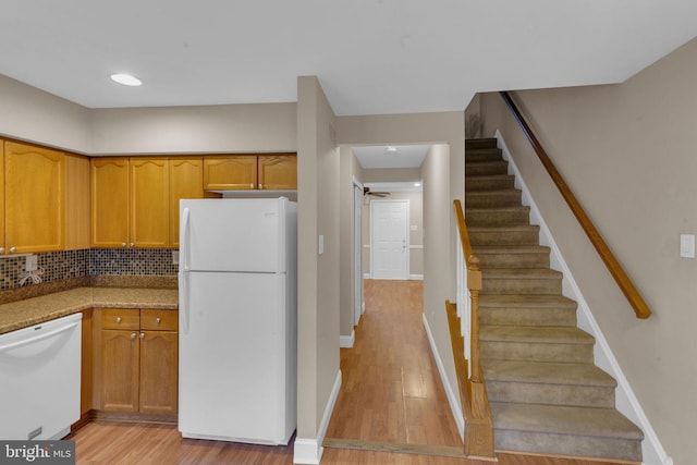 kitchen with white appliances, light stone countertops, light hardwood / wood-style floors, and backsplash