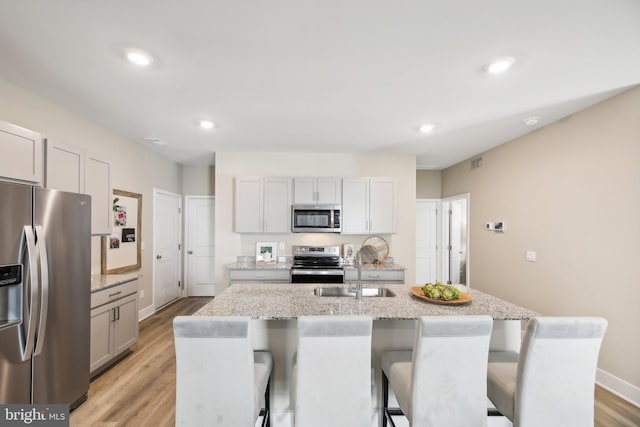 kitchen with a breakfast bar, sink, light stone countertops, an island with sink, and appliances with stainless steel finishes