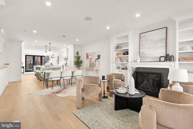 living room featuring built in shelves, light wood-type flooring, ornamental molding, recessed lighting, and a glass covered fireplace