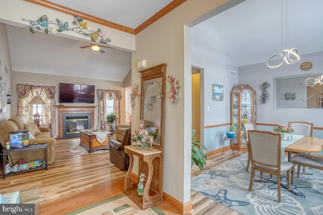 dining space with crown molding, vaulted ceiling, ceiling fan with notable chandelier, and hardwood / wood-style flooring